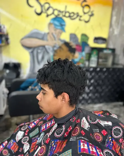 Jovem com cabelo cacheado e degradê, de perfil