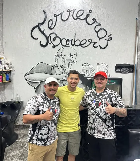 Os barbeiros da Ferreira ao lado do jogador Matheus, em frente ao grafite da barbearia