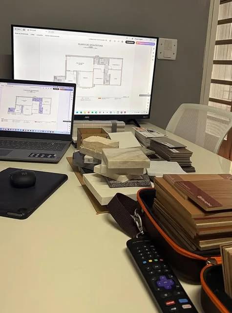 Mesa de trabalho com plantas na tela e amostras de materiais
